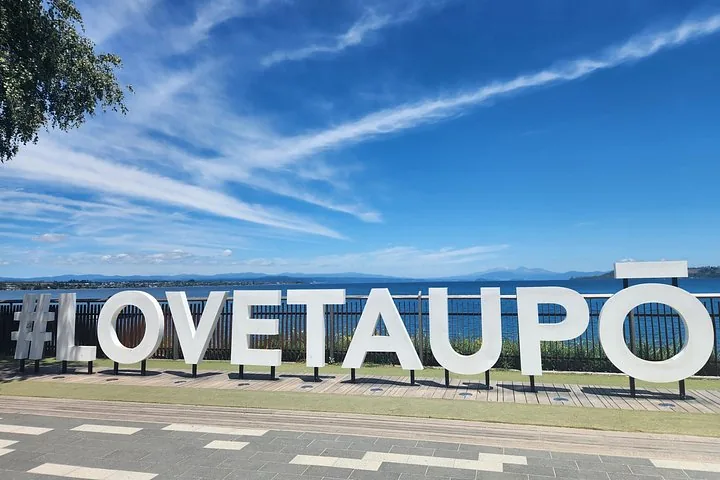 Grande enseigne blanche #LOVETAUPO surplombant un lac bleu calme