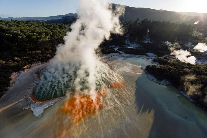 Luchtfoto van een stomende geothermische poel met oranje randen bij Wai-O-Tapu.