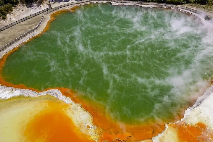 Großes grünes geothermisches Becken mit orangefarbenen Rändern und aufsteigendem Dampf, Luftaufnahme.